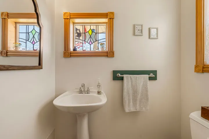Pedestal sink with chrome faucet, stained glass window, and wood-framed mirror