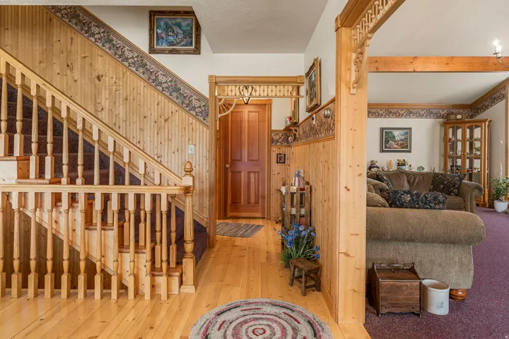 Wood-finish flooring, wood paneling, wood staircase with balusters, wood door, and decorative wood archway