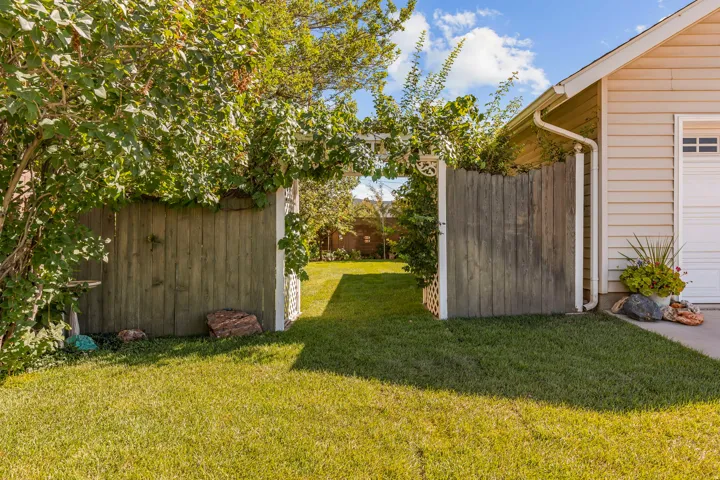 Manicured lawn, wooden privacy fencing, and a white trellis gate
