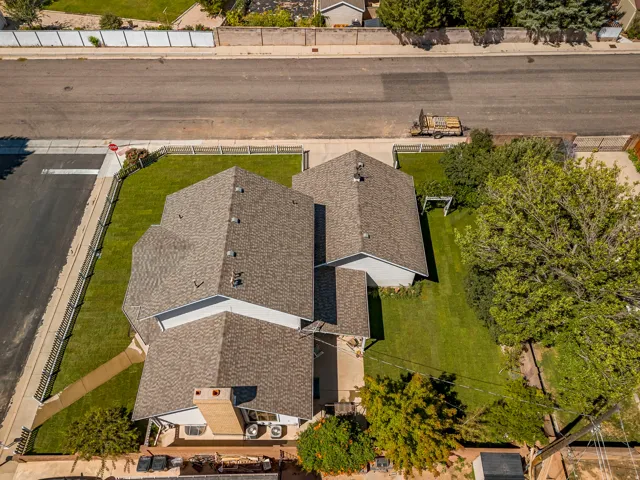 Pitched shingle roof, well-maintained lawn, multiple mature trees, concrete sidewalks, and a brick chimney