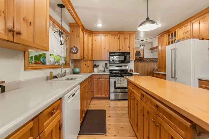 Kitchen featuring extensive wood cabinetry, light-toned countertops, stainless steel appliances, a center island with a wood surface, and recessed lighting