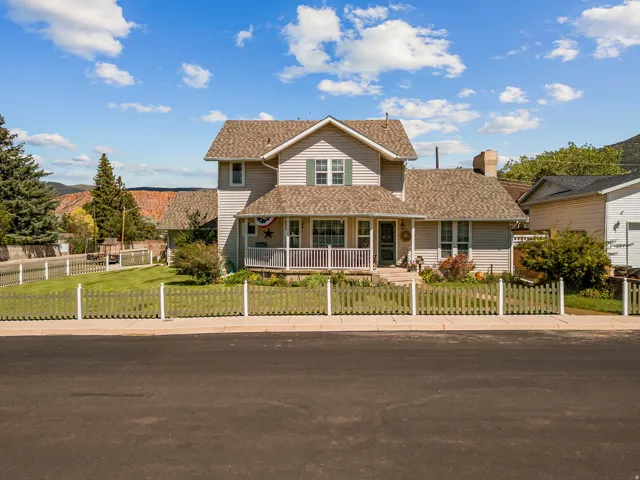 Two-story home with light-colored siding, a covered front porch, and a white picket fence enclosing the front yard