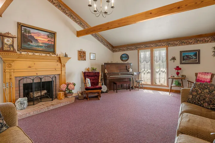 Vaulted ceiling with exposed wood beams, brick fireplace with wood mantel, and multiple windows providing natural light