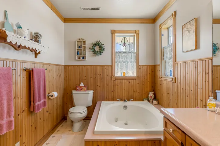 Built-in jetted tub, wood paneling, light wood window frames, decorative window glass, and light wood cabinetry
