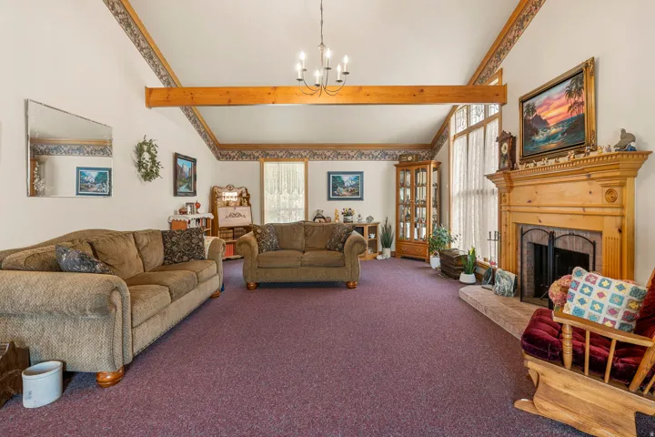 Vaulted ceiling with exposed wood beam, wood-finish fireplace mantel with stone hearth, large window with transom, and built-in display cabinetry