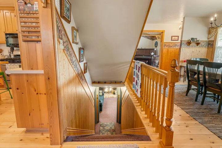 Wood-finish flooring throughout, wood paneling on walls, wood staircase with balusters, built-in kitchen cabinetry, and a dining area with a chandelier