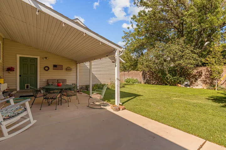 Covered concrete patio with overhead lighting, featuring a green exterior door and tan siding