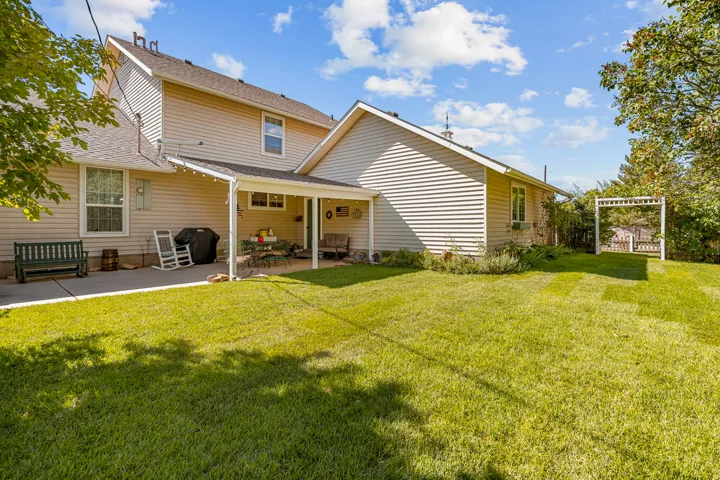 Expansive lawn area with a covered patio, additional concrete patio, and a decorative garden arbor