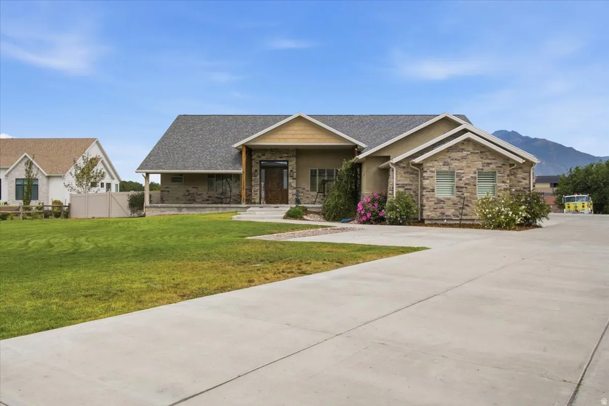 Stone and stucco exterior, covered front porch, concrete driveway, front lawn, and mature landscaping