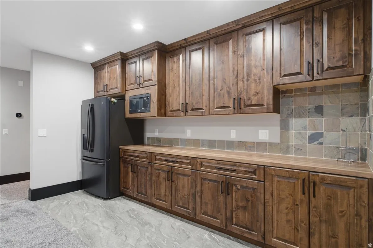 Custom cabinetry with dark hardware, stone tile backsplash, wood-finish countertops, and recessed lighting