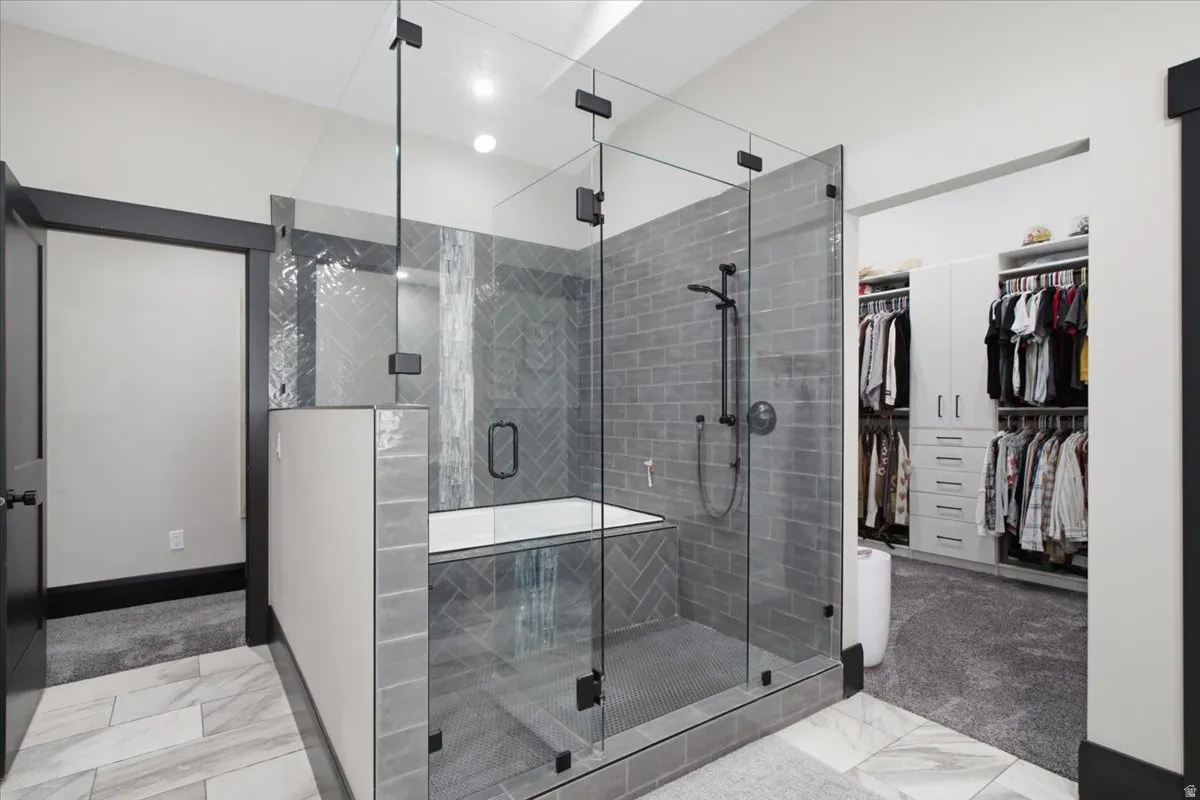Glass-enclosed shower with matte black fixtures, gray subway tile, and a built-in bench