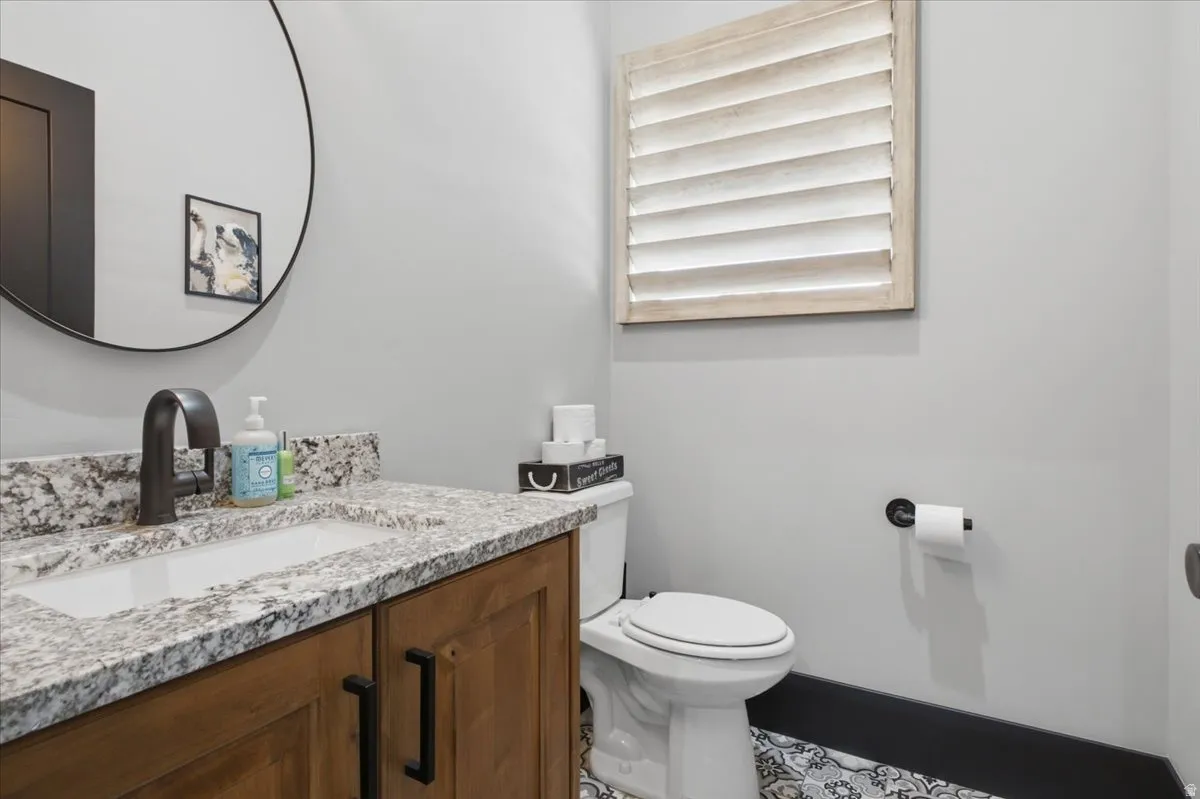 Wood-finish vanity with dark hardware, undermount sink, and stone countertop