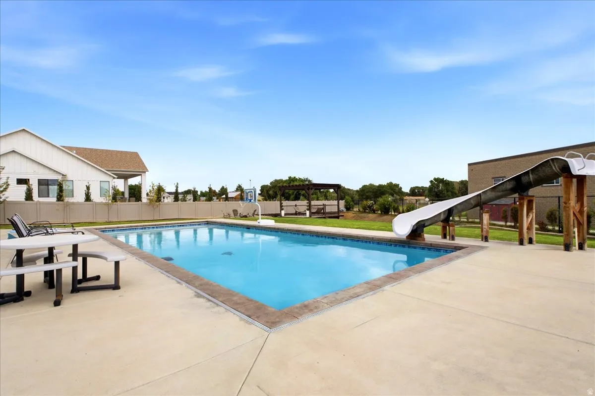 In-ground swimming pool with a concrete surround, an attached water slide, and a nearby wooden pergola