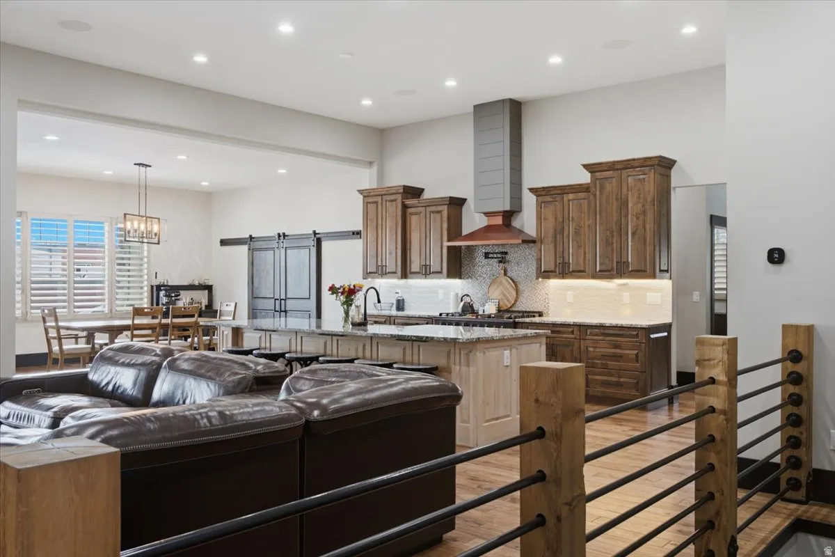 Open-concept living area with wood-finish flooring, a kitchen island with seating, dark wood cabinetry, and a range hood featuring a metallic accent