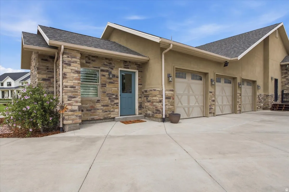 Exterior featuring stone and stucco siding, a three-car garage with carriage-style doors, and a concrete driveway
