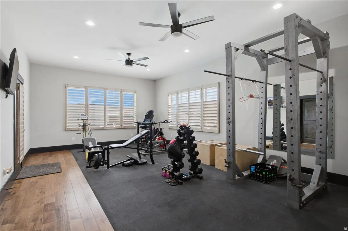 Spacious room featuring multiple windows with plantation shutters, wood-finish flooring, recessed lighting, and dual ceiling fans