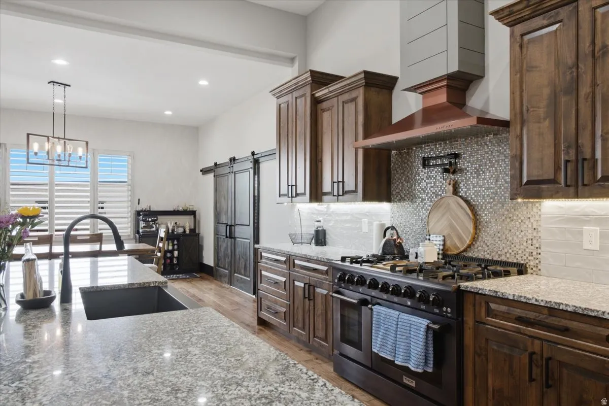 Spacious kitchen featuring granite countertops, dark wood cabinetry, a built-in range with a custom hood, a mosaic tile backsplash, and a large kitchen island with an undermount sink