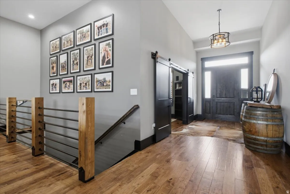 Wood-finish flooring, dark wood entry door with transom and sidelights, overhead drum pendant light, and dark wood barn doors