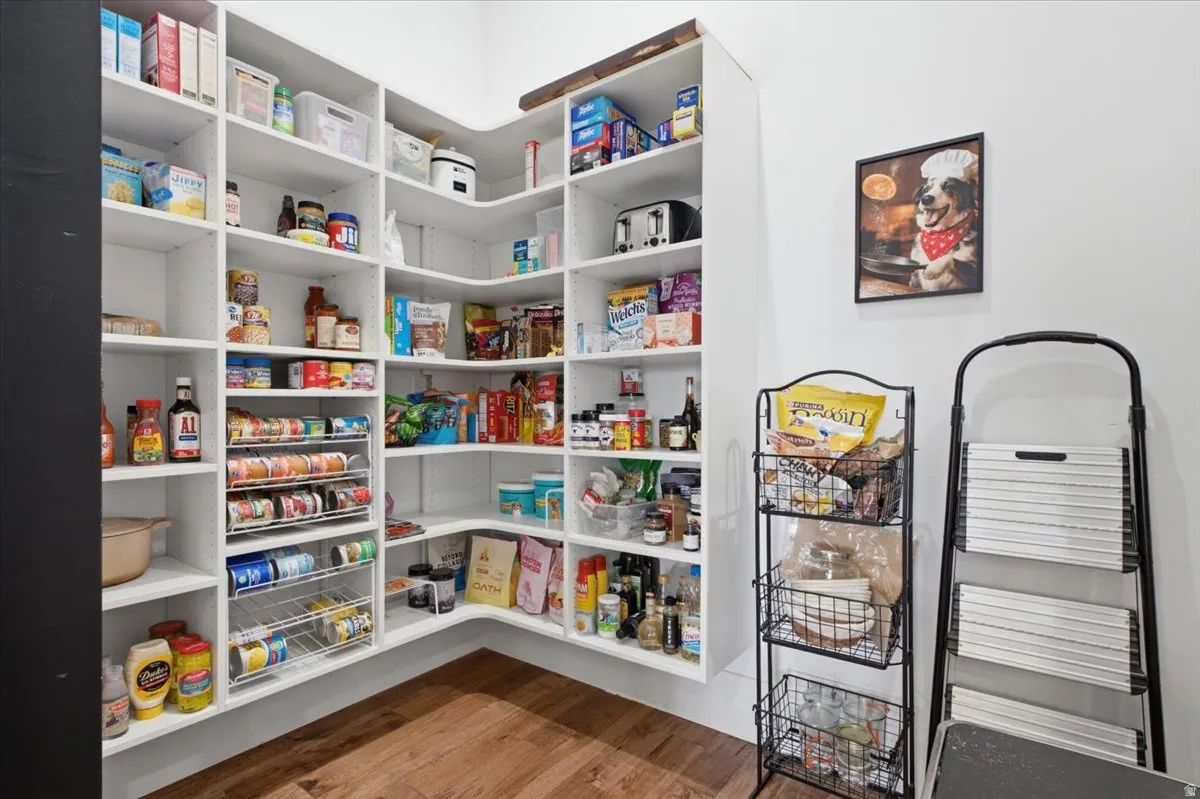 Expansive walk-in pantry featuring white built-in shelving, integrated can dispensers, and wood-finish flooring