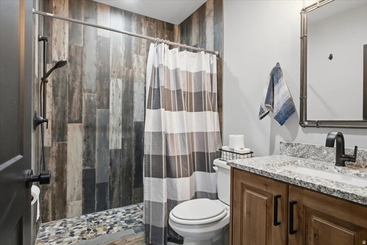 Contemporary bathroom featuring a walk-in shower with slate-look tile surround and mosaic floor inlay, a white ceramic toilet, and a wood-finish vanity with a speckled quartz countertop