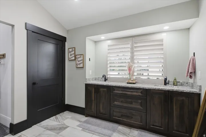 Dual vanity with stone countertop and integrated sinks, dark wood-finish cabinetry, and plantation shutters