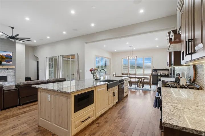 Gourmet kitchen featuring a large center island with wood cabinetry and integrated microwave, quartz countertops, stainless steel appliances, recessed and pendant lighting, and hardwood flooring throughout the open-concept living space