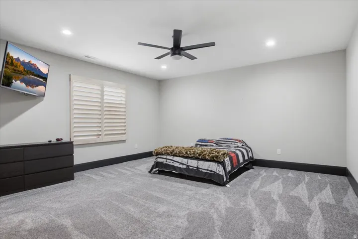 Recessed lighting, ceiling fan, wide baseboards, window with plantation shutters, and patterned carpet