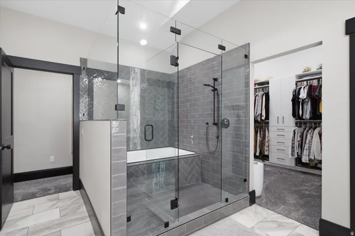 Glass-enclosed shower with matte black fixtures, gray subway tile, and a built-in bench