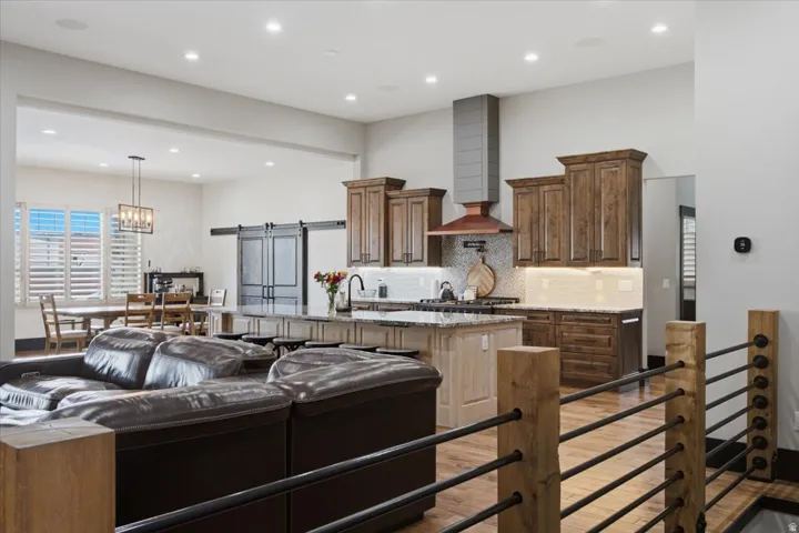 Open-concept living area with wood-finish flooring, a kitchen island with seating, dark wood cabinetry, and a range hood featuring a metallic accent