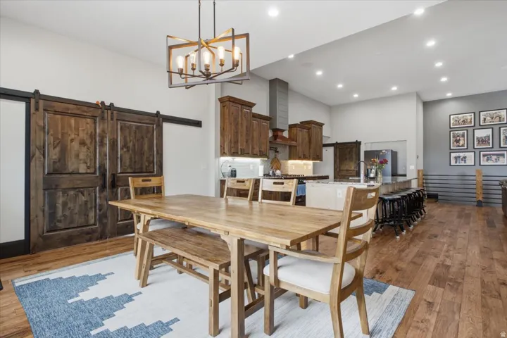 Hardwood flooring, wood-finish barn doors, recessed lighting, island with seating, and a modern chandelier
