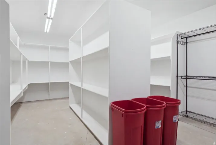 Walk-in pantry featuring extensive built-in shelving, concrete flooring, and overhead strip lighting