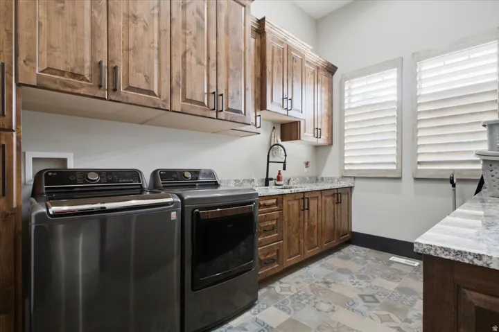 Laundry room featuring rich wood cabinetry, patterned tile flooring, a utility sink with a matte black faucet, and plantation-style window shutters