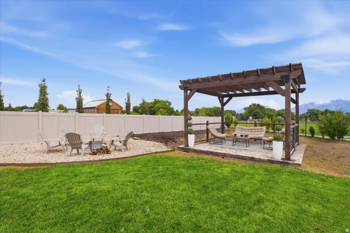 Expansive backyard featuring a manicured lawn, a gravel fire pit area, a wooden pergola, and a privacy fence