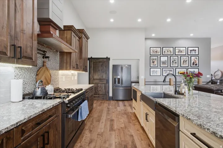 Kitchen featuring wood-finish flooring, granite countertops, wood cabinetry, a stainless steel range, and a farmhouse sink with a matte black faucet
