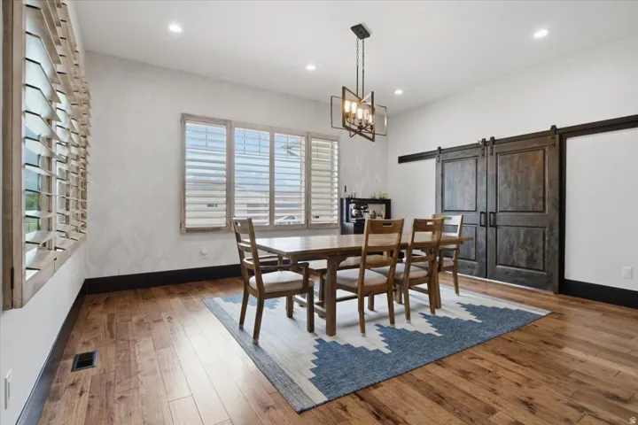 Hardwood flooring, recessed lighting, wood plantation shutters, modern linear chandelier, and wood barn doors