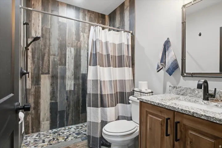 Contemporary bathroom featuring a walk-in shower with slate-look tile surround and mosaic floor inlay, a white ceramic toilet, and a wood-finish vanity with a speckled quartz countertop