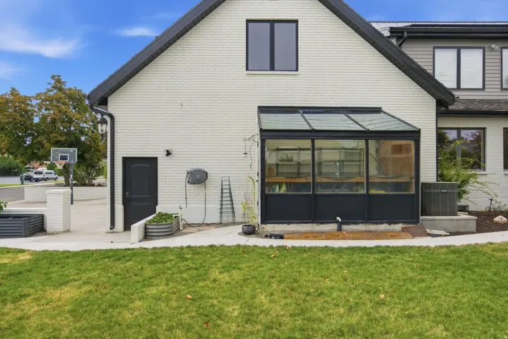 White brick exterior with dark trim, featuring a sunroom addition and a concrete patio