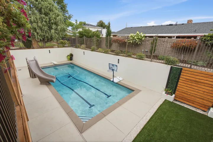 In-ground swimming pool with a diving board, surrounding concrete patio, and slatted wood privacy screen