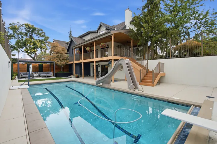 Rear exterior featuring an inground swimming pool, diving board, and terraced wood deck with stairs