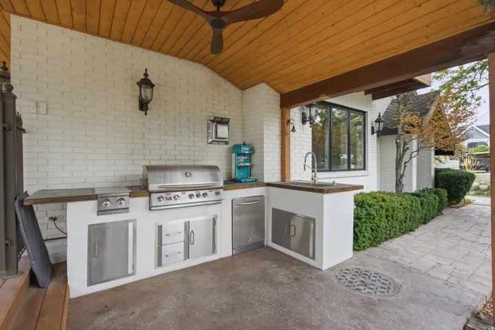 Outdoor kitchen featuring a built-in grill, stainless steel cabinetry, and a sink with a gooseneck faucet