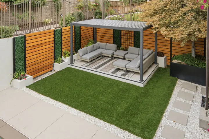 Outdoor living area featuring a modern pergola, horizontal wood-paneled privacy fence, integrated planters, and a manicured lawn