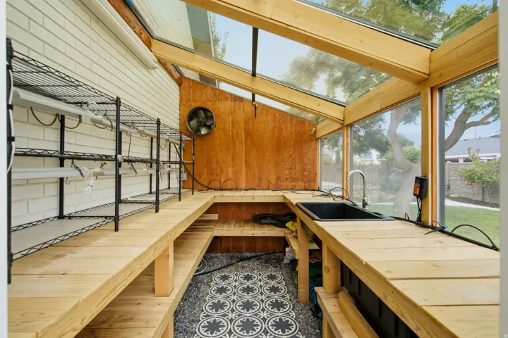 Greenhouse structure featuring extensive wood-finish shelving, integrated sink with faucet, white brick wall, and patterned floor tiles