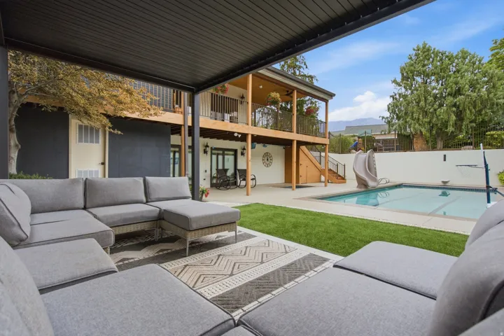 Covered patio with a black slatted ceiling, expansive lawn, swimming pool, concrete pool deck, and multi-level wood deck