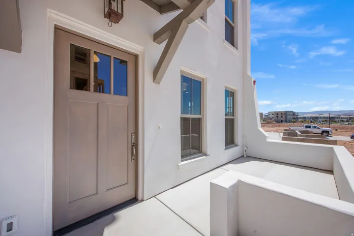 Exterior entry featuring a light-toned door with glass panels, an overhead sconce, and an exterior patio with a low wall