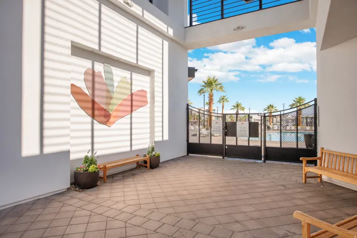 Paved walkway with a decorative wall feature and an ornate metal gate providing access to a pool area with palm trees