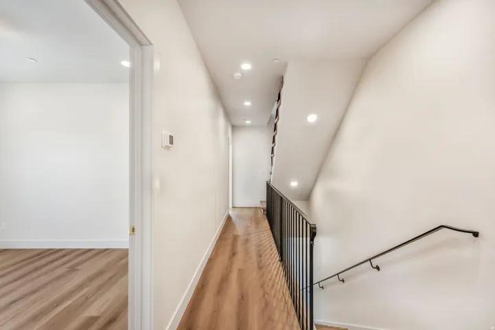 Hallway with wood-finish flooring, recessed lighting, and a contemporary black metal staircase railing