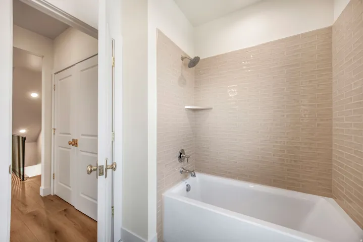 Built-in bathtub with subway tile surround, integrated shower fixture, and a wall-mounted corner shelf