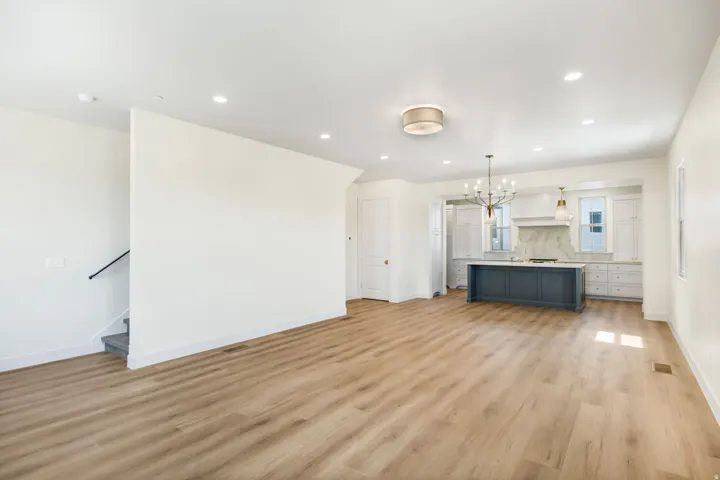 Wood-finish flooring throughout, recessed lighting, and a kitchen featuring a central island with a contrasting finish, white cabinetry, and a full-height backsplash