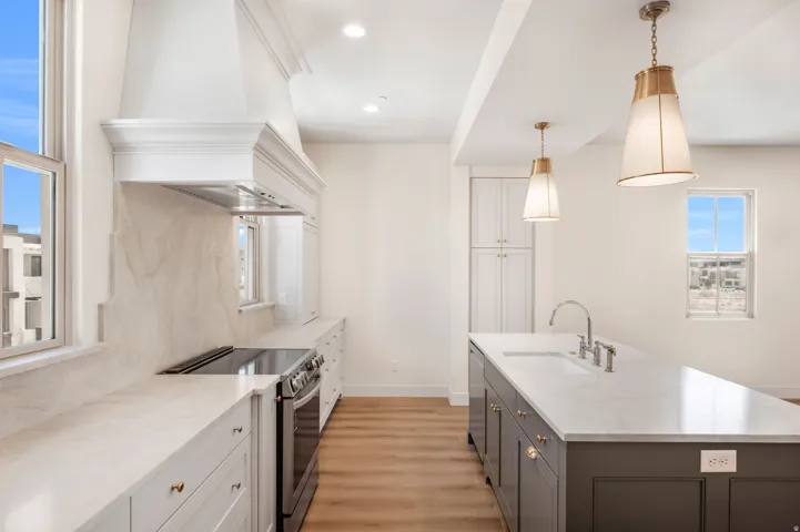 Expansive kitchen featuring a custom range hood, stone countertops, wood-finish flooring, and a large island with an integrated sink