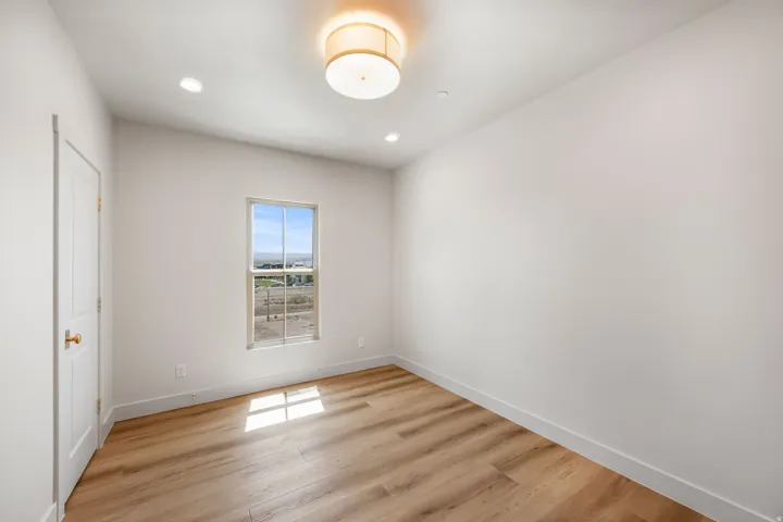 Wood-finish flooring, recessed lighting, and a drum ceiling fixture illuminate this room with a white paneled door